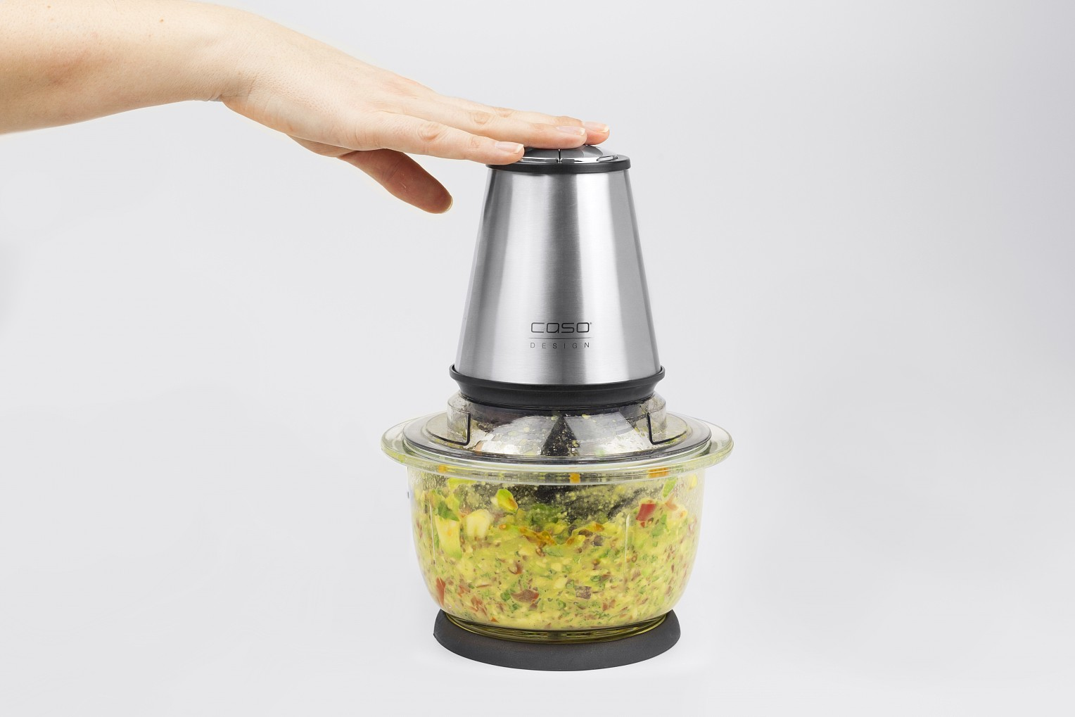 Silberner Foodprocessor mit Hand oben. Schüssel enthält gehacktes Gemüse, weißer Hintergrund.