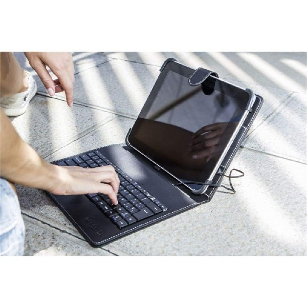 Una tableta con una funda de teclado sobre una superficie de piedra, con una mano escribiendo.