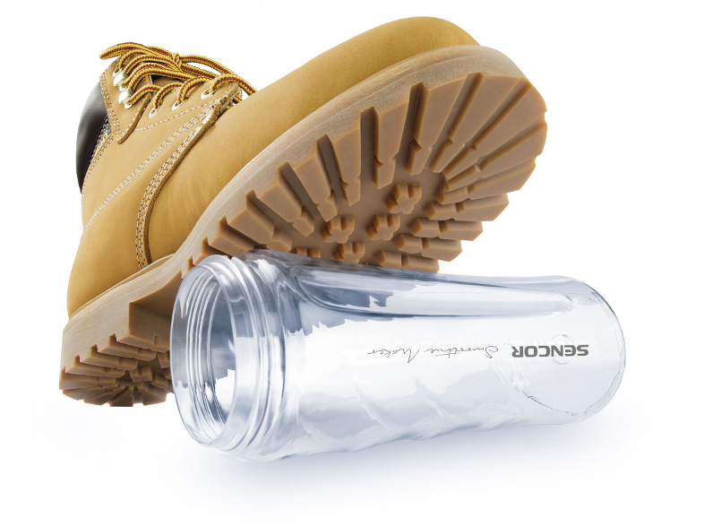 Sárga munkásbakancs felfelé néző talppal, egy átlátszó smoothie készítő palack mellett.