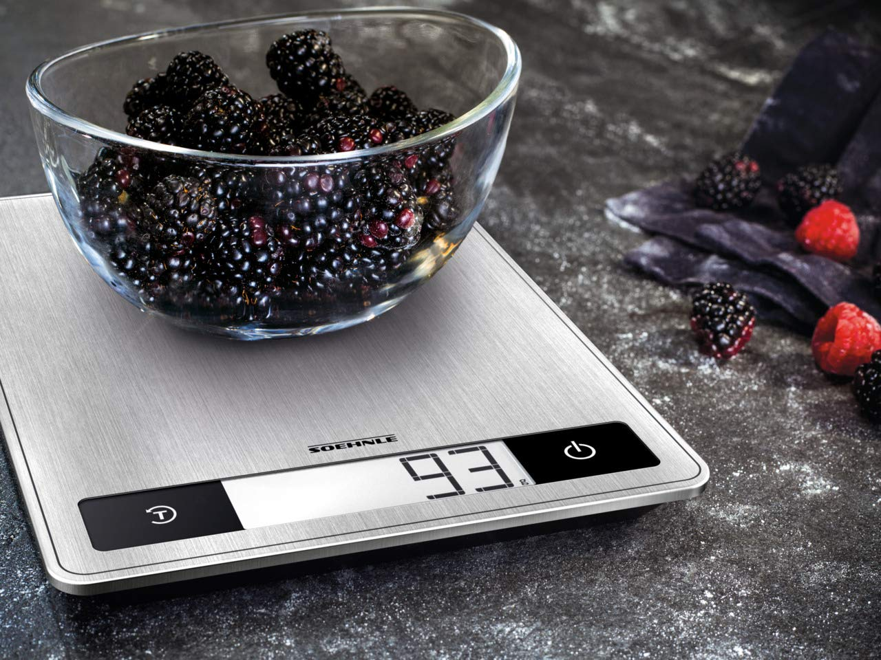 Glasschale mit Brombeeren auf einer Waage. Digitalanzeige zeigt 93. Beeren und ein Tuch sind sichtbar.