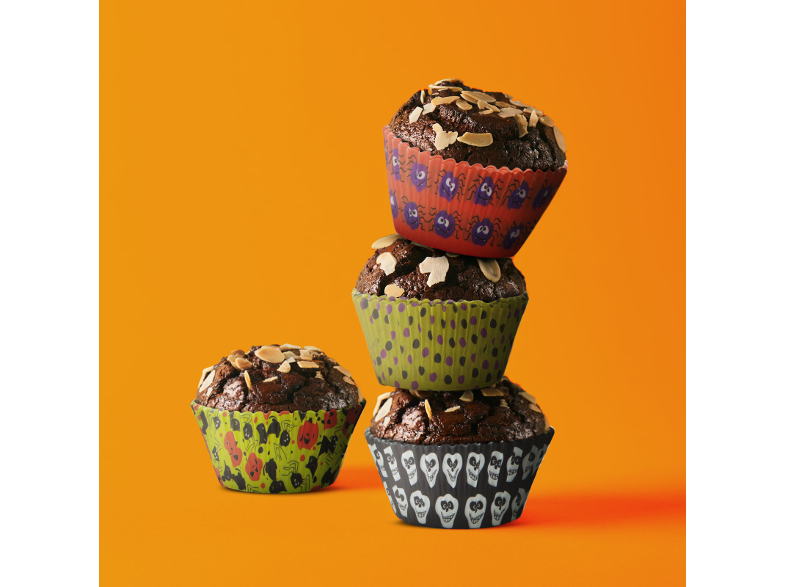 Négy Halloween muffin különböző díszített papírral. Narancssárga háttéren egymásra rakva.