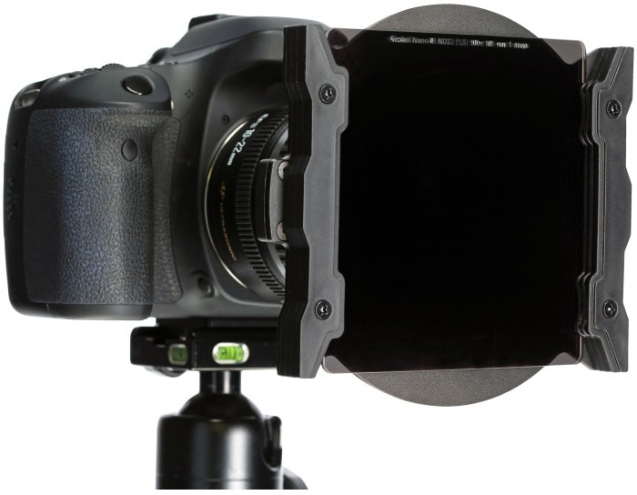 A camera with a lens filter attached to a tripod. The filter is black, and the camera is black.