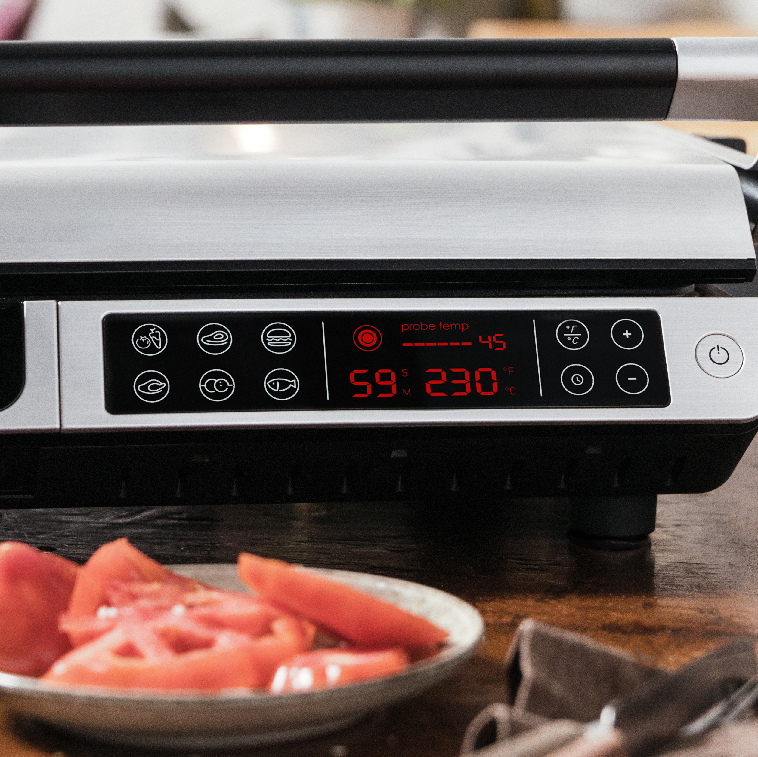 Grill mit digitaler Anzeige. Tomaten im Vordergrund. Edelstahl-Finish.