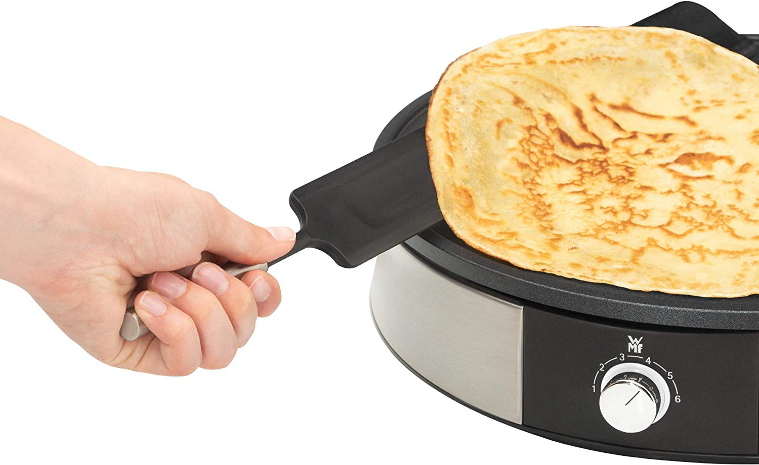 Frittella che viene girata su una piastra nera. Mano tiene una spatola nera con manico argentato.
