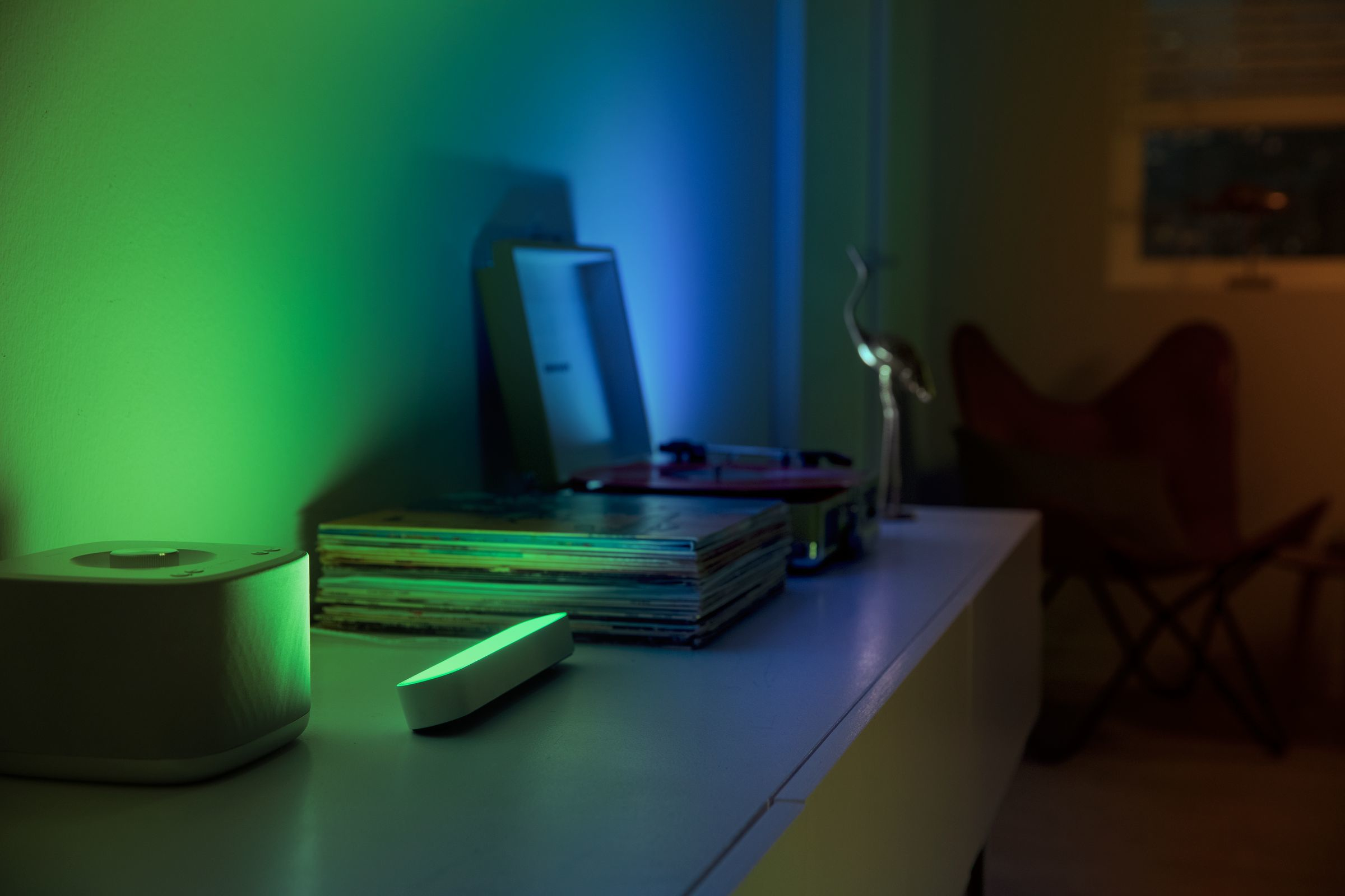 A table has a speaker, a record player, and records. Lighting creates green and blue hues.