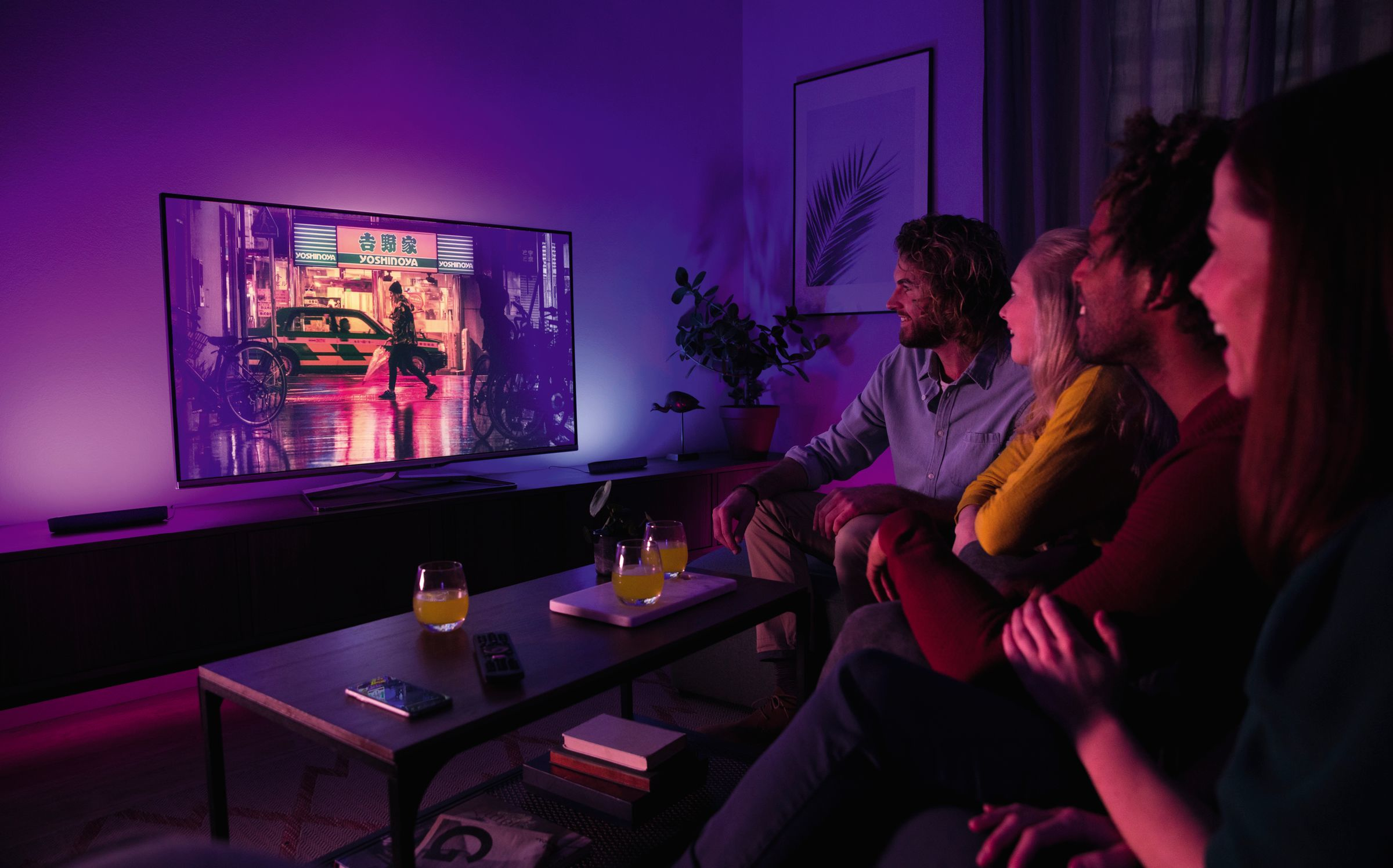 Un gruppo di persone guarda la TV con un'illuminazione ambientale colorata.