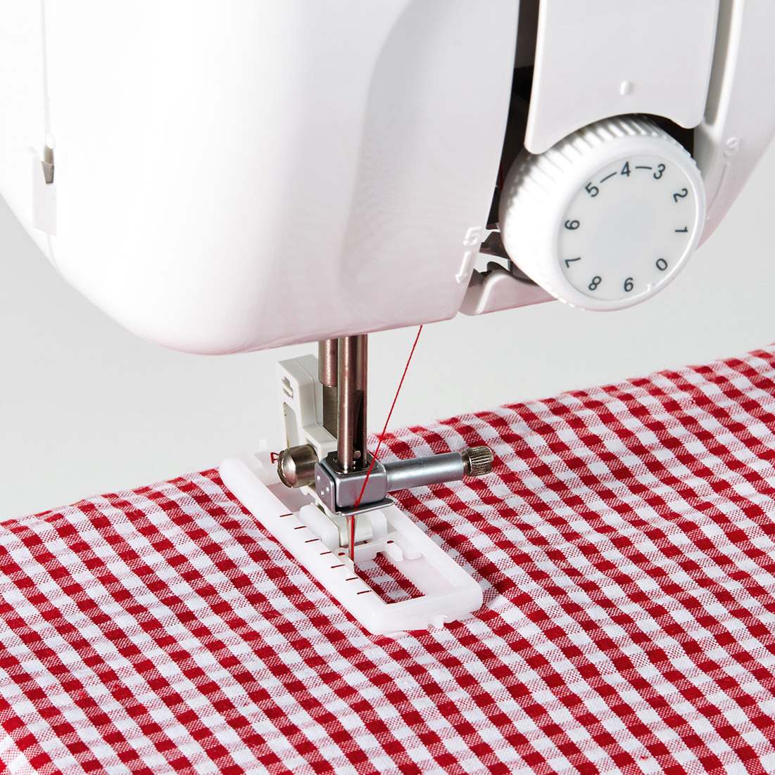 Detail der Nähmaschine. Roter Faden, karierter Stoff und ein weißer Nähfuß.