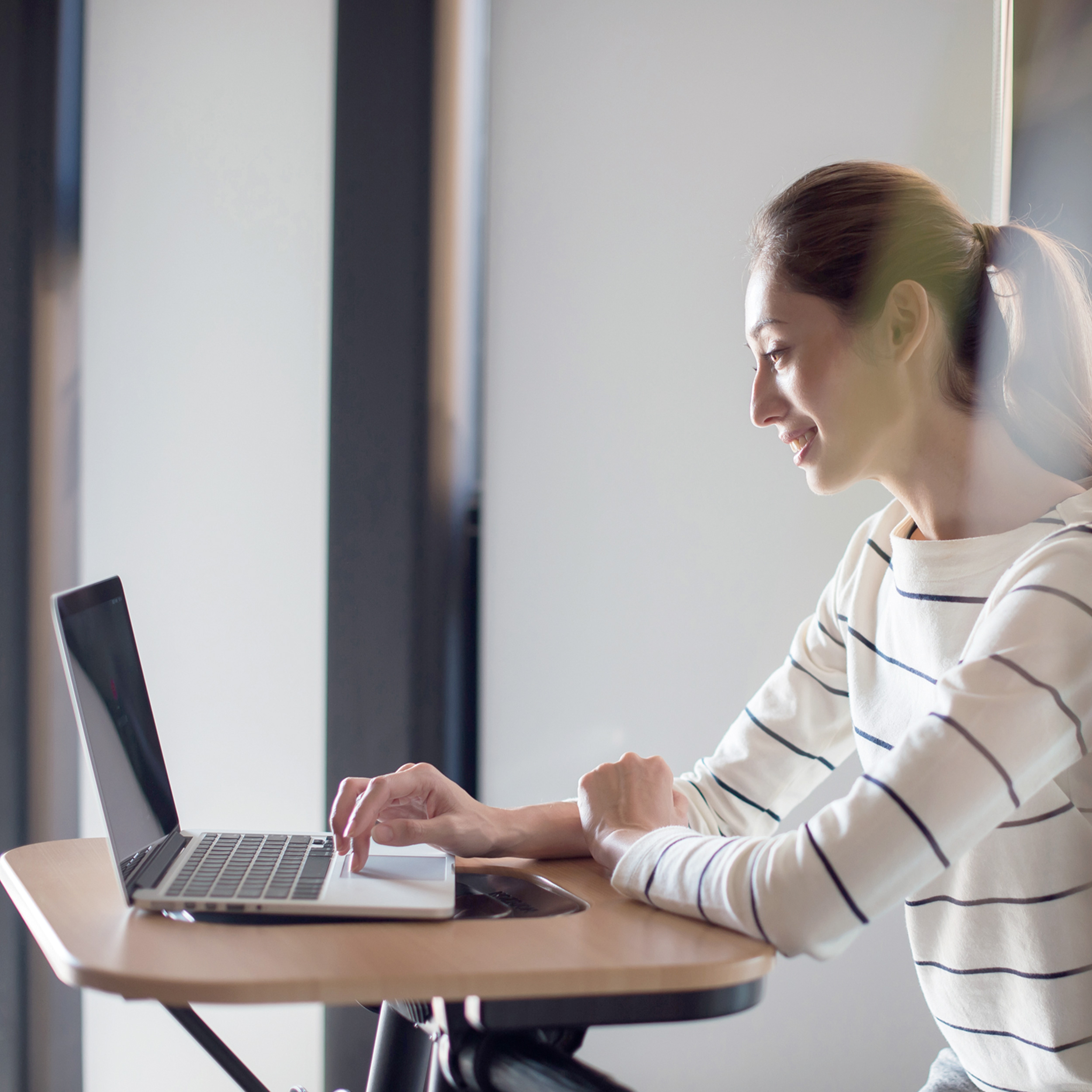 Eine Frau, die an einem Laptop an einem Stehpult arbeitet und lächelt.