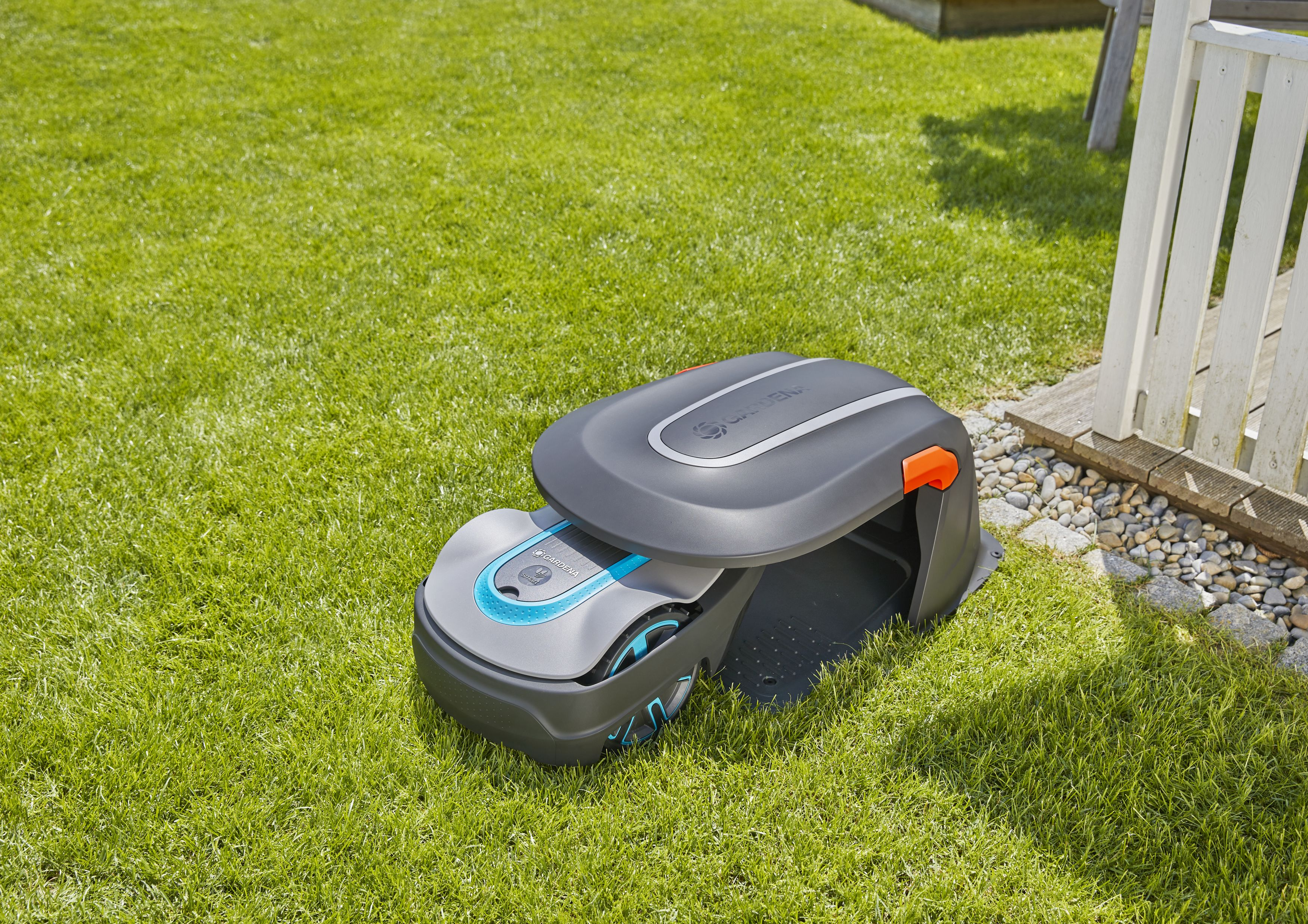Robot-Rasenmäher auf Gras, weißer Zaun und Haus im Hintergrund.