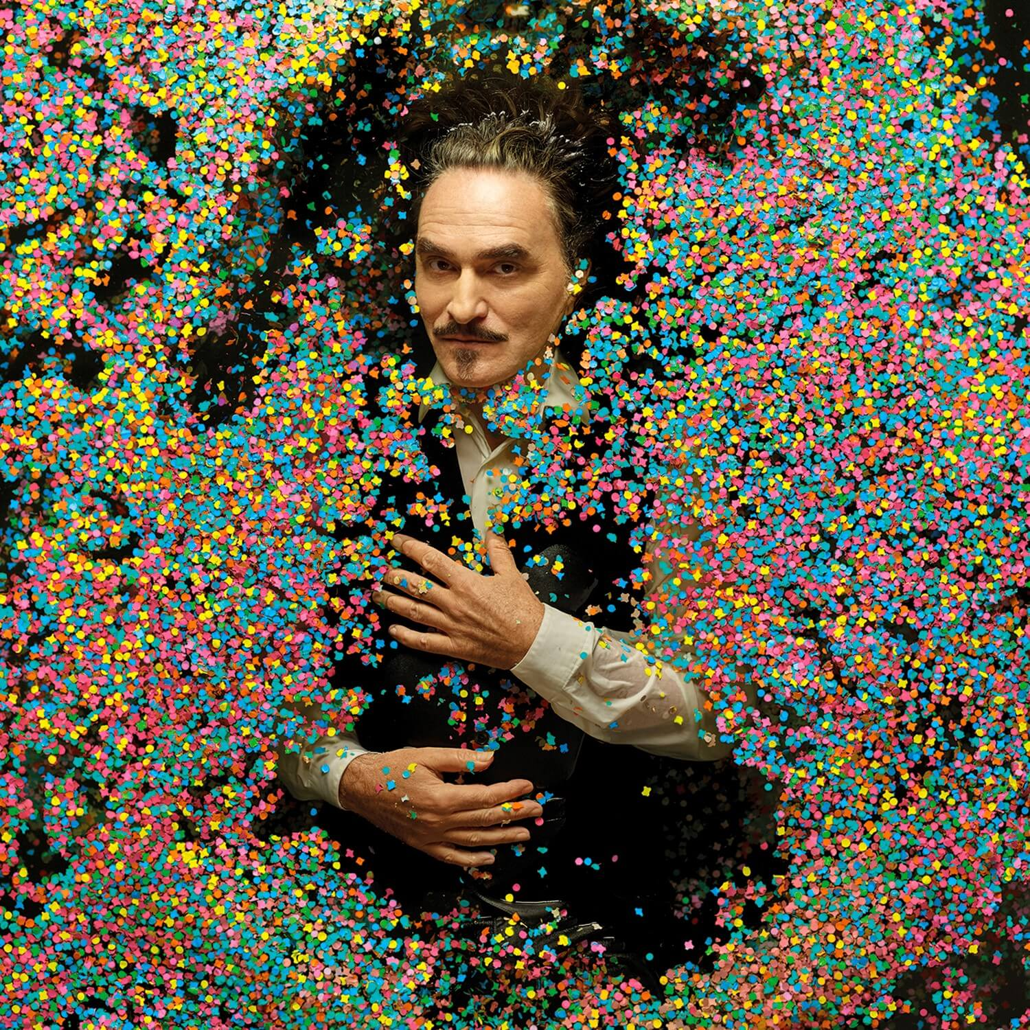 Man in pak liggend in kleurrijke confetti, kijkt naar de kijker.