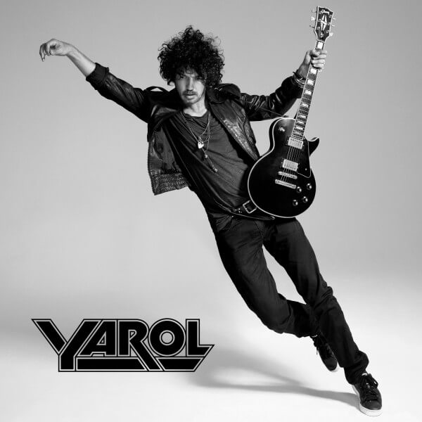Photo en noir et blanc d'un homme aux cheveux bouclés, veste en cuir, tenant une guitare.