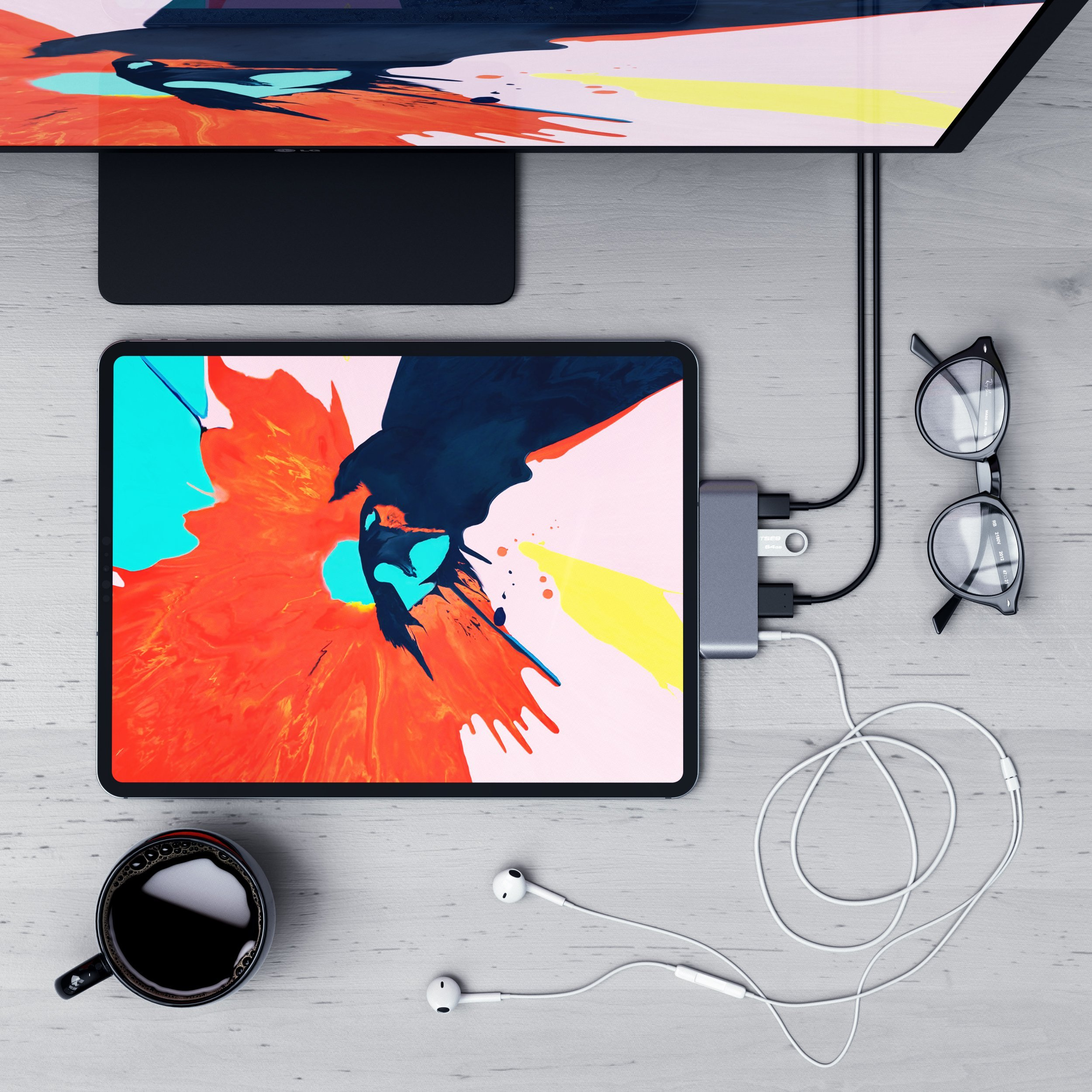 Ein Tablet, Monitor, Brille, Kopfhörer, Tasse Kaffee und ein USB-Hub auf einem Holztisch.