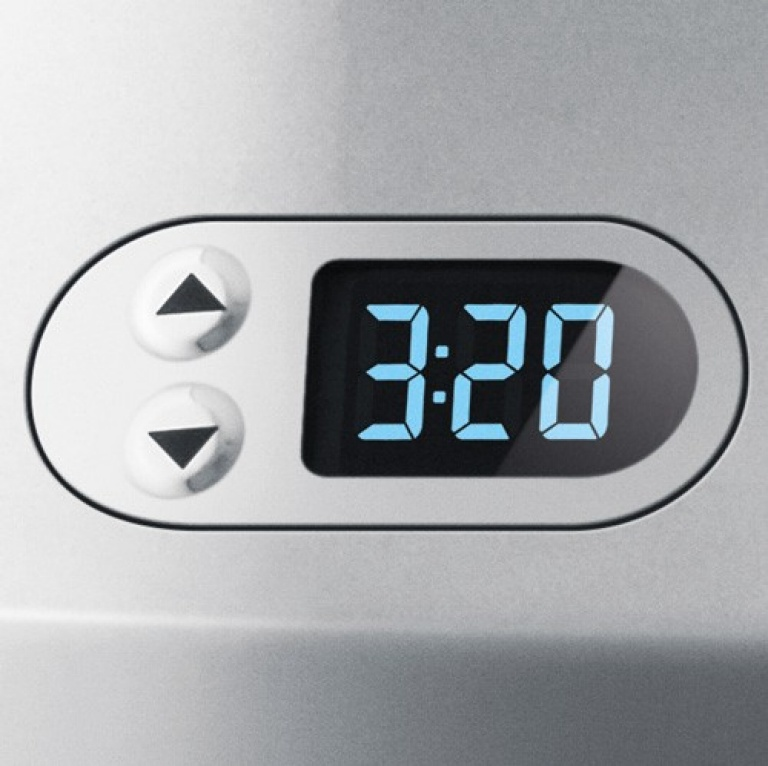 Eine Digitaluhr zeigt 3:20 in blauen Ziffern an. Zwei Knöpfe mit Pfeilen befinden sich links.