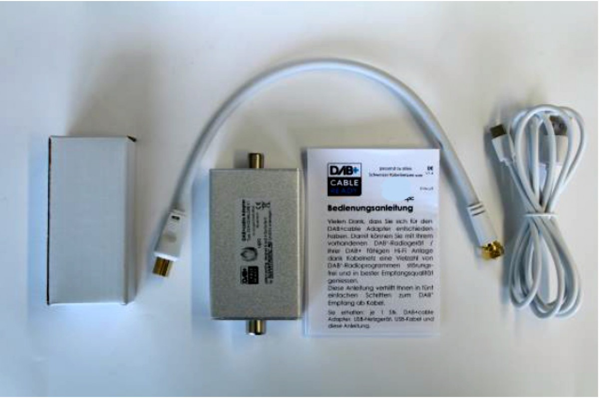 Un adaptateur de câble DAB+ avec accessoires, un câble blanc et un manuel sur une surface.
