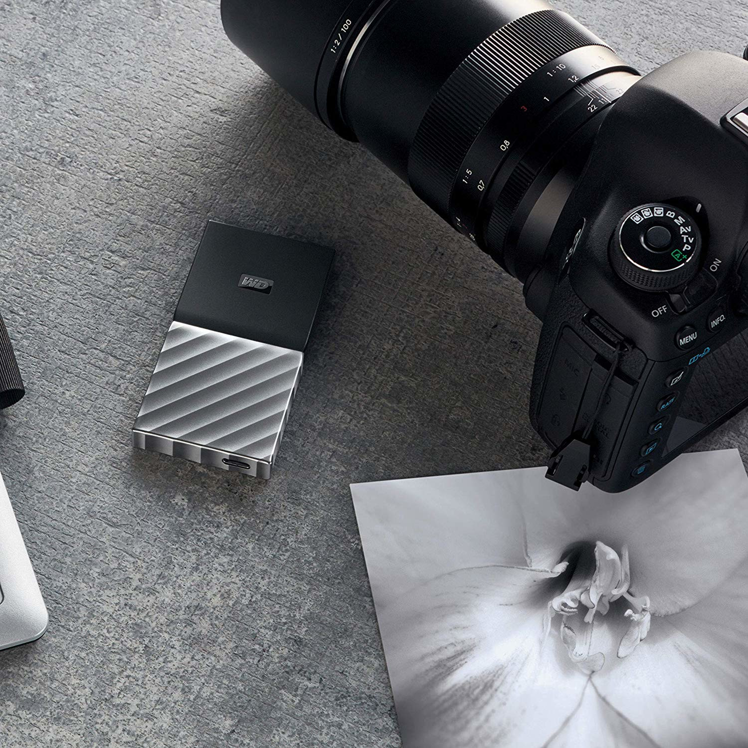 Silver external hard drive next to a camera and a photo. Gray surface.