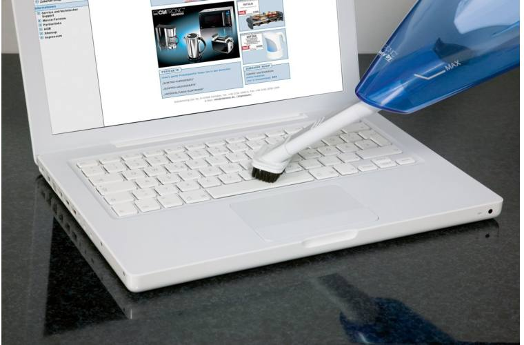 Laptopot kézi porszívóval tisztítanak. A billentyűzet a fókuszban.