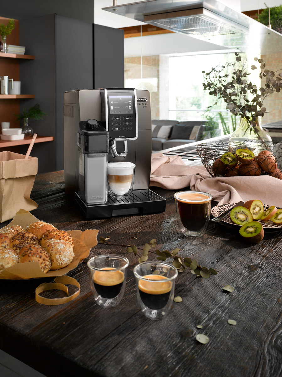 Eine Kaffeemaschine, zwei Espressotassen und Essen auf einem Holztisch. Die Umgebung ist drinnen.