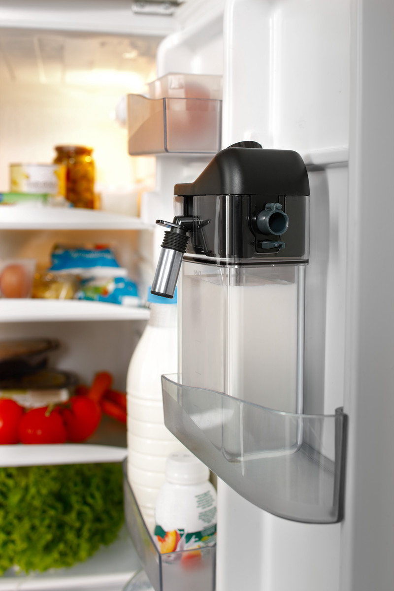 In einem Kühlschrank ist ein schwarz-transparenter Milchspender an der Tür montiert, Milch und Tomaten sind sichtbar.