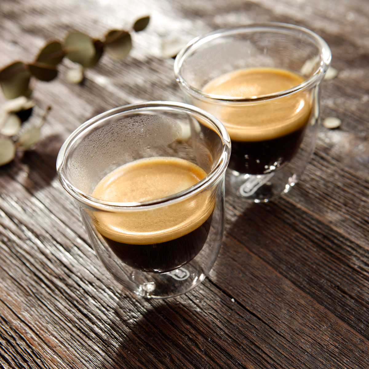 Zwei durchsichtige Gläser mit Espresso, die auf einer Holzoberfläche stehen.