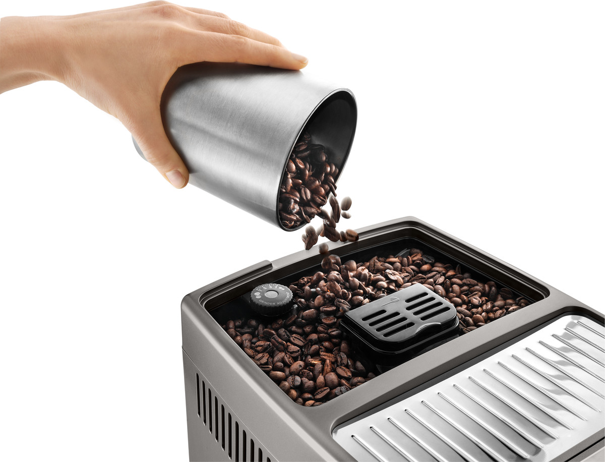 Eine Hand gießt Kaffeebohnen aus einem silbernen Behälter in eine Kaffeemaschine.