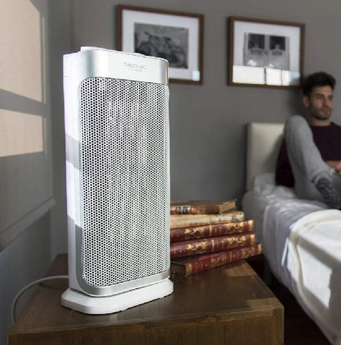 Un calentador eléctrico blanco y plateado sobre una mesa de madera, con un hombre al fondo.