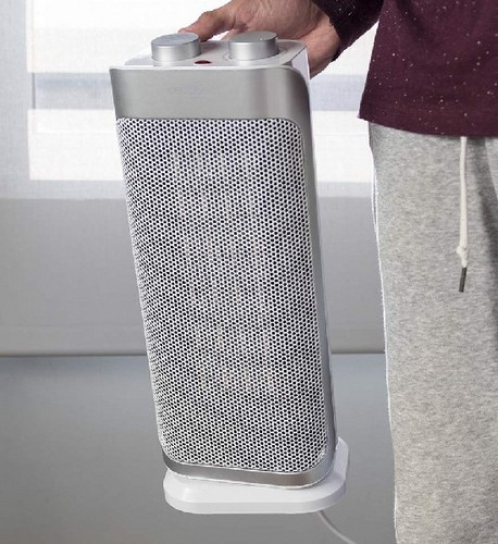 Un hombre sostiene un calefactor eléctrico blanco y plateado. El calefactor está sobre base blanca.