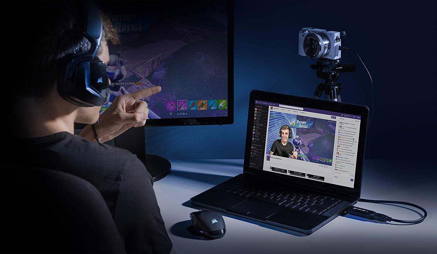 Eine Person spielt, streamt auf einem Laptop mit Kamera und einem Monitor, der das Spiel zeigt.