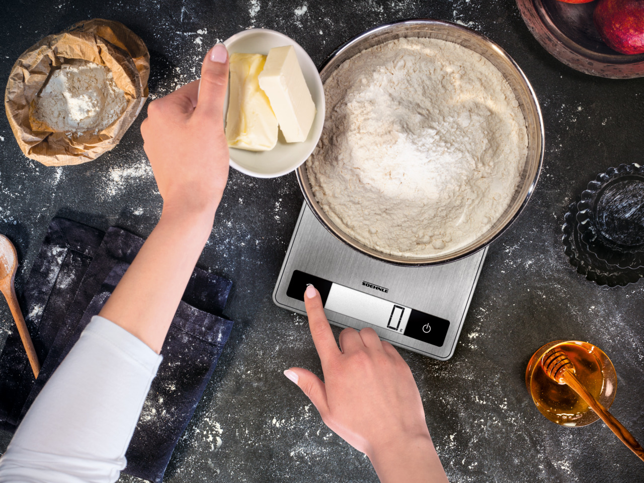 Eine Person, die eine digitale Küchenwaage benutzt, mit Butter und Mehl in der Nähe.