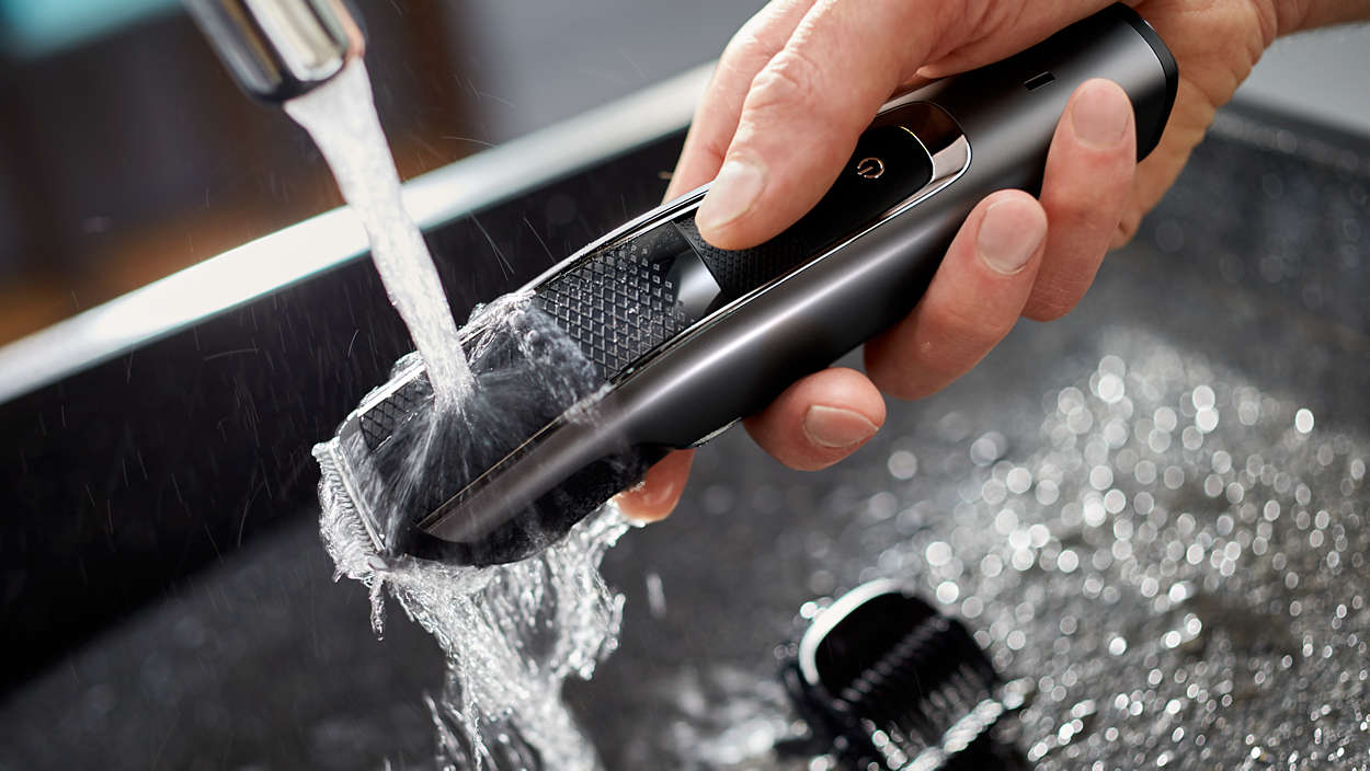 Hand hält einen schwarzen Philips Haarschneider unter fließendem Wasser in einem Waschbecken.