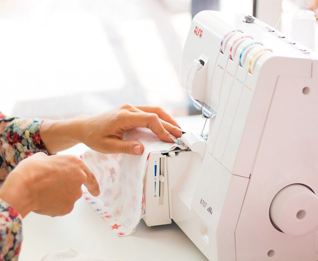 Una persona cosiendo tela con una máquina de coser blanca. Las manos son visibles.