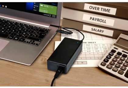 Laptop e caricatore su una scrivania. Buste paga, stipendio e straordinari sullo sfondo.