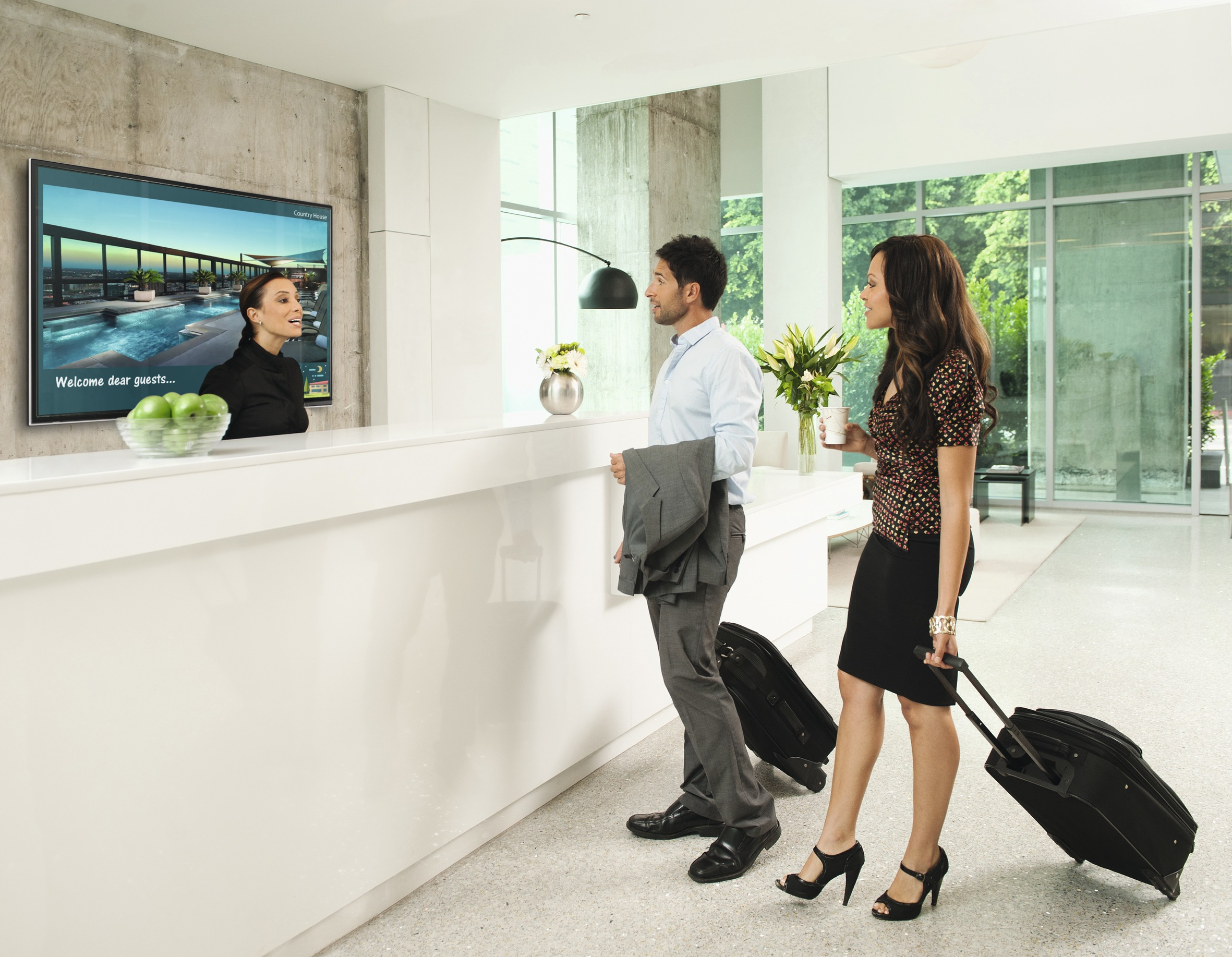 Escena de vestíbulo de hotel con recepcionista, pareja con equipaje y pantalla de bienvenida.
