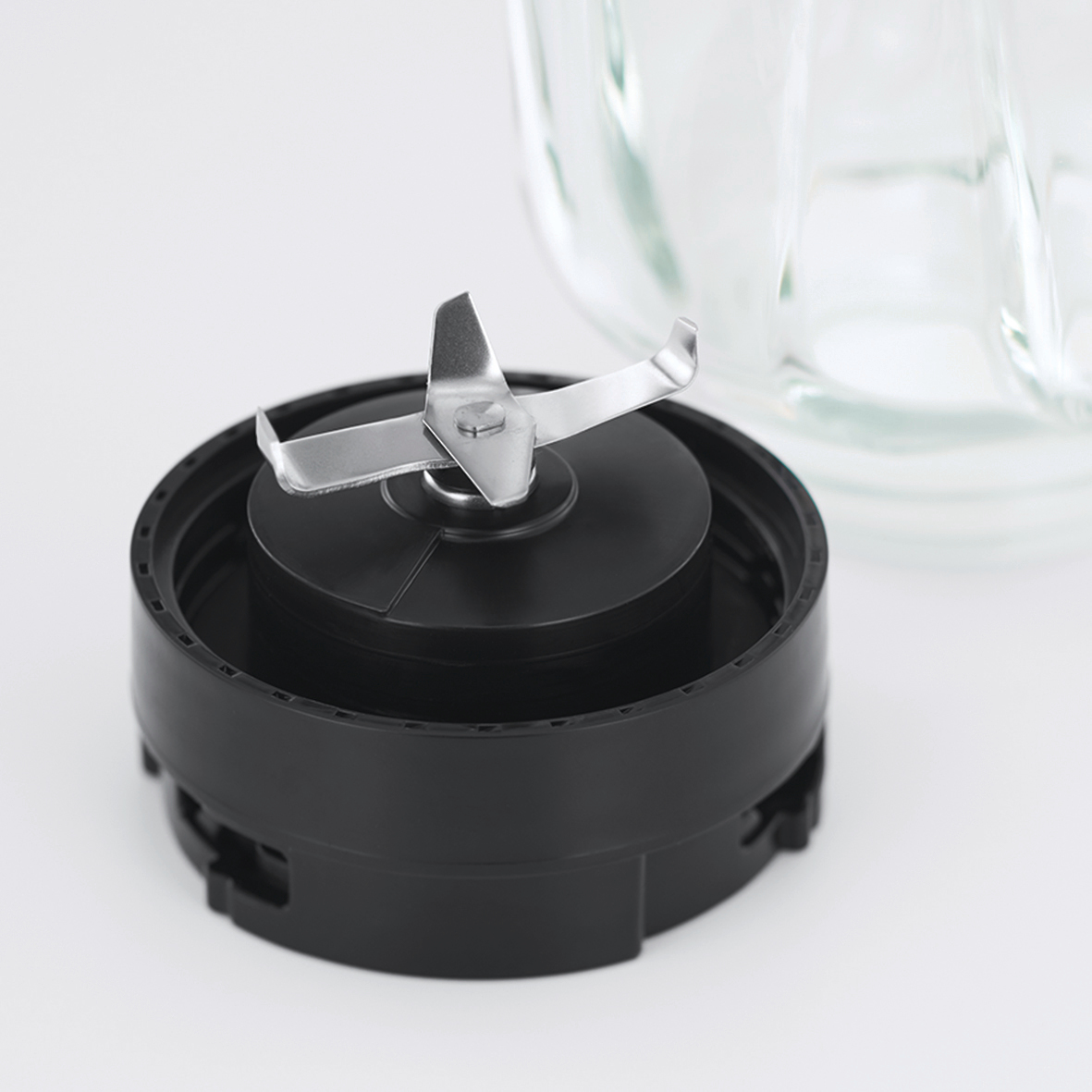 Schwarze Mixer-Klinge an schwarzer Basis, mit Glasbehälter im Hintergrund.