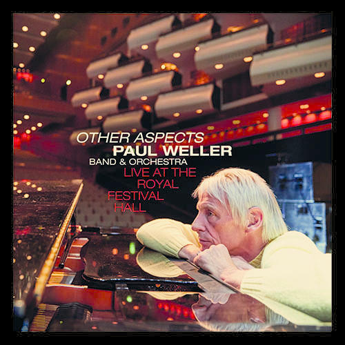 Paul Weller albumhoes. Hij leunt op een piano, in een concertzaal.