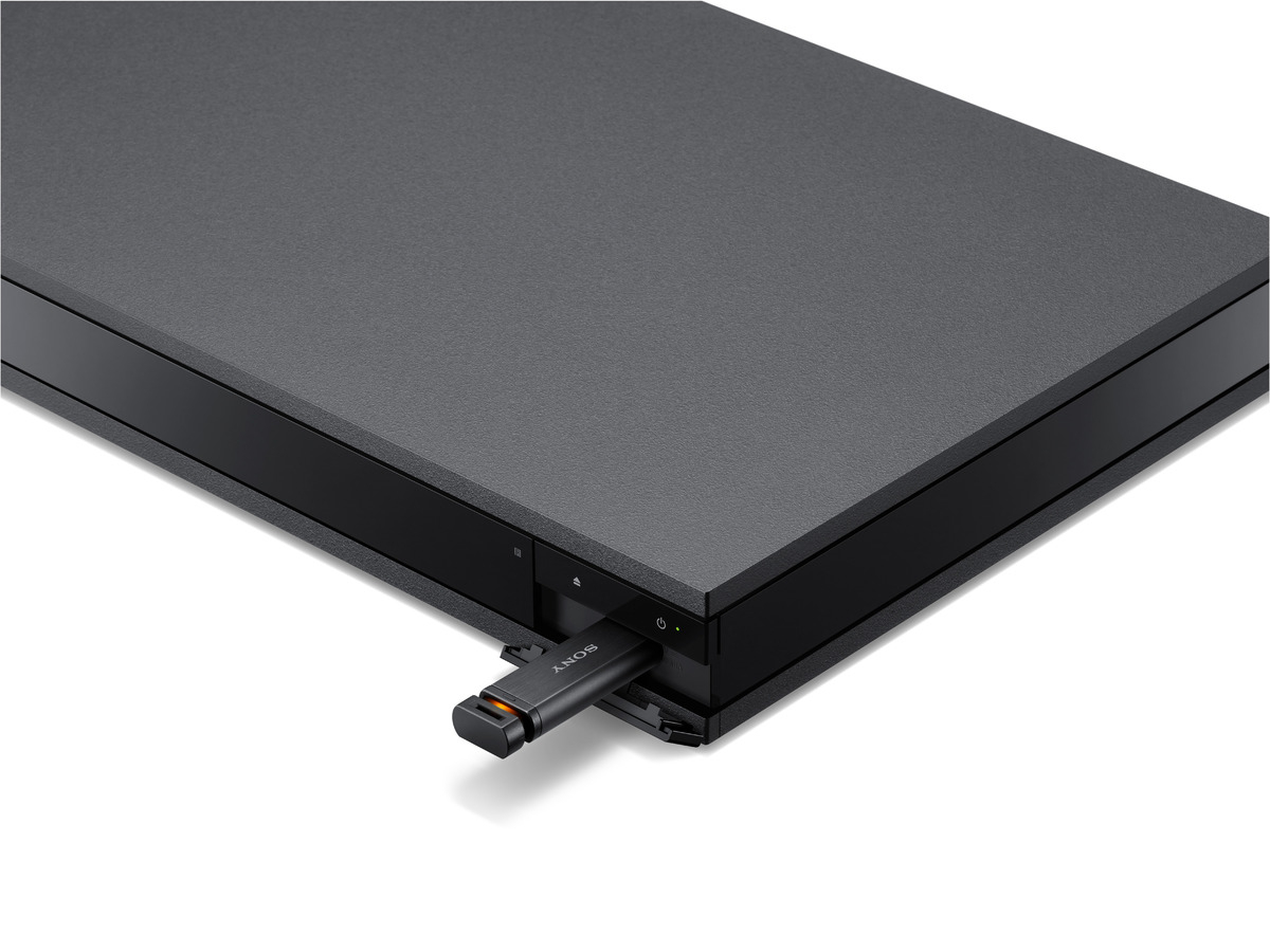 Schwarzer Sony Blu-ray-Player mit eingestecktem USB-Laufwerk auf weißer Oberfläche, mit Ein-/Aus-Taste.