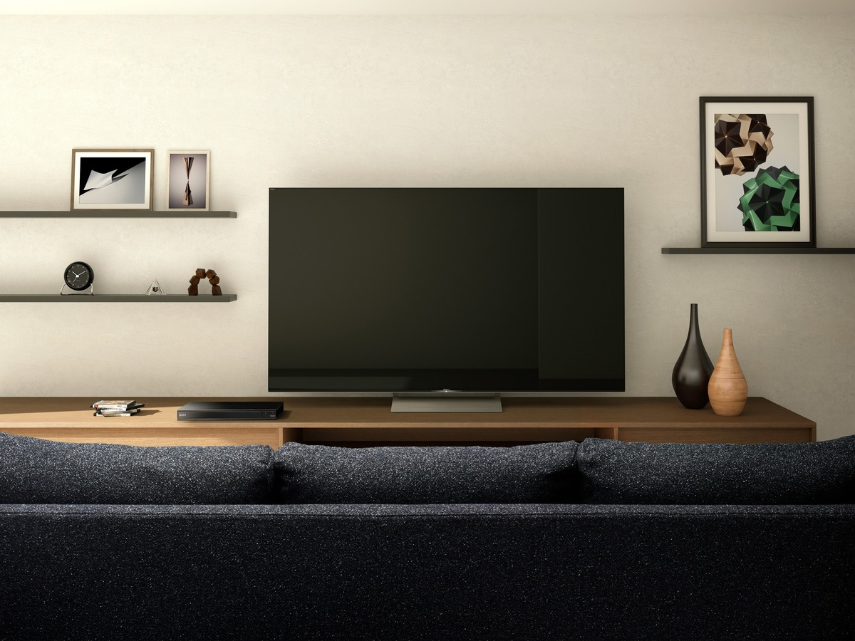 Ein modernes Wohnzimmer mit einem Fernseher auf einem Holzschrank, einer Couch und dekorativen Gegenständen auf Regalen.