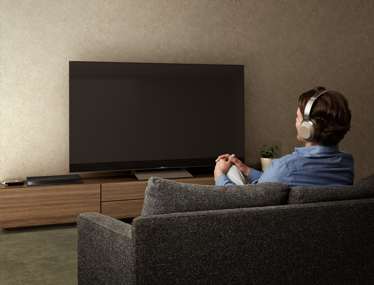 Mann mit Kopfhörern schaut TV auf Couch. Soundbar unter TV, im Wohnzimmer.