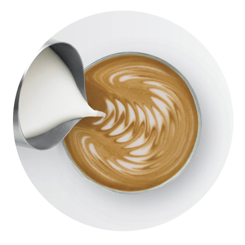 Milch wird in eine Tasse Kaffee gegossen, wodurch Latte Art entsteht.