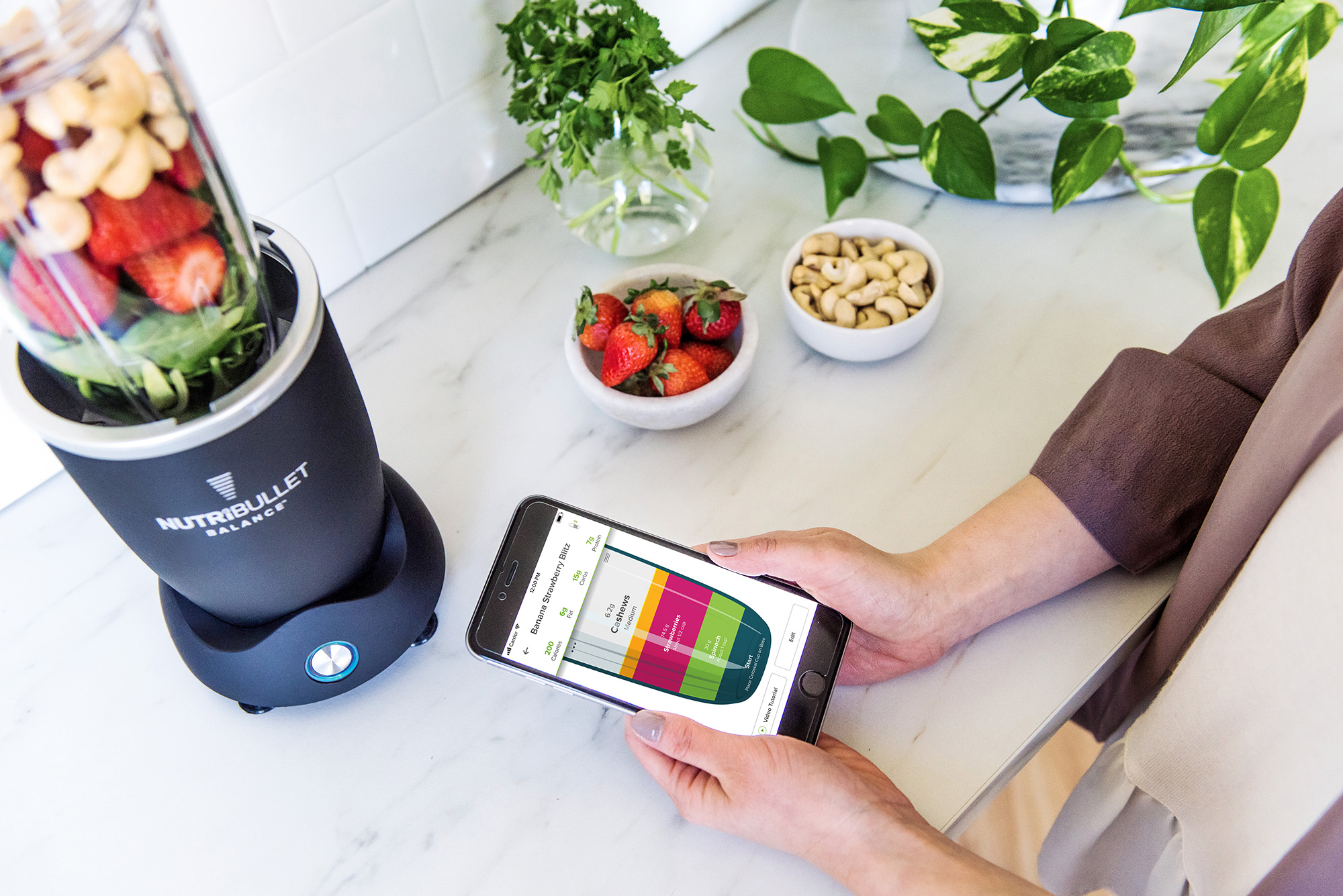 Een blender en telefoon met een smoothie-recept op het scherm en ingrediënten.