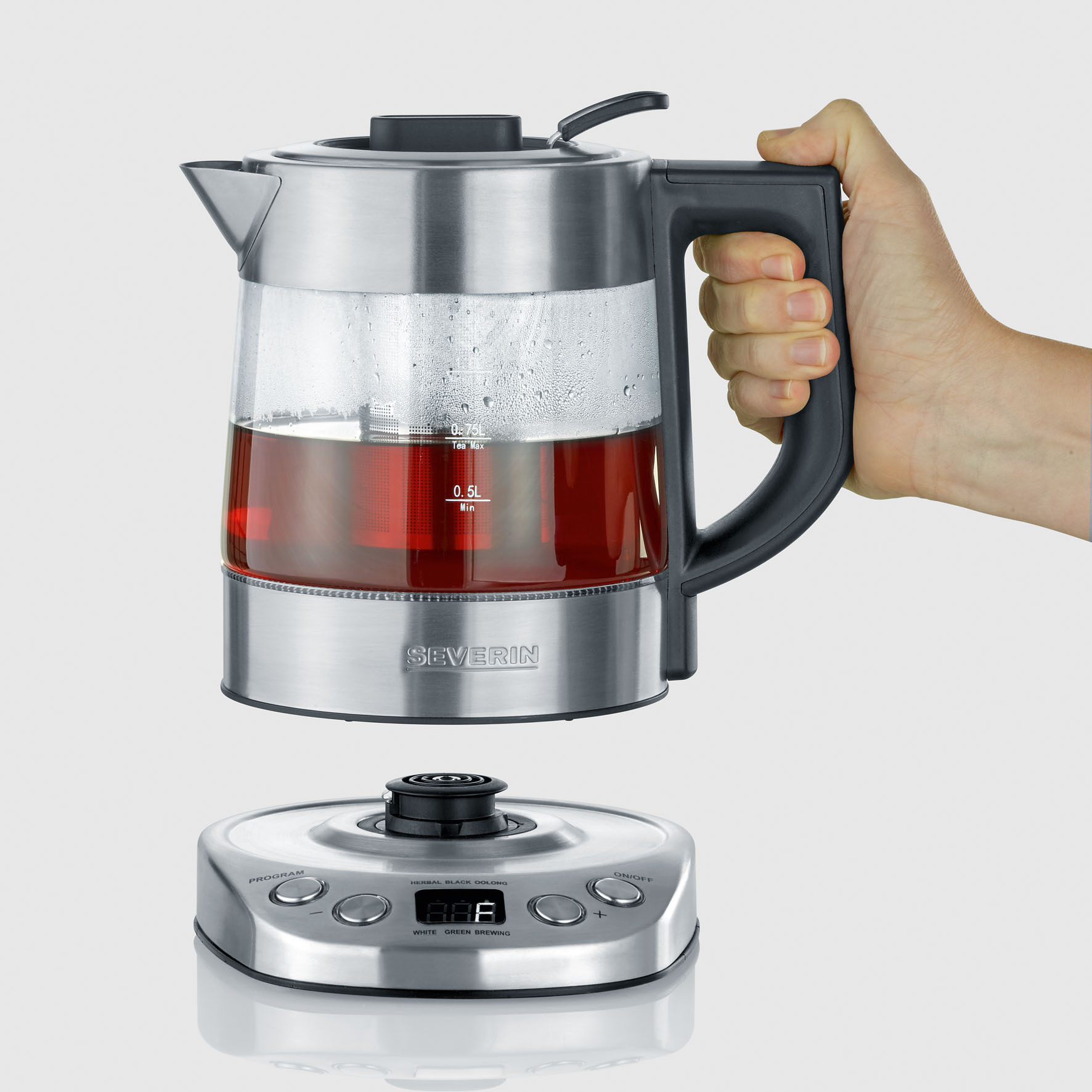 Waterkoker, glas met rode vloeistof, op voet. Hand op de handgreep.