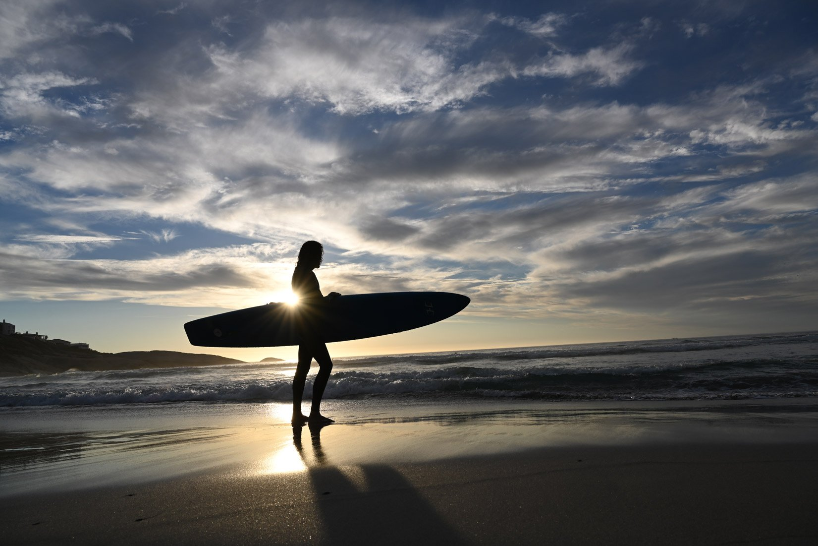 Silhouette d'un surfeur tenant une planche de surf sur une plage au coucher du soleil.