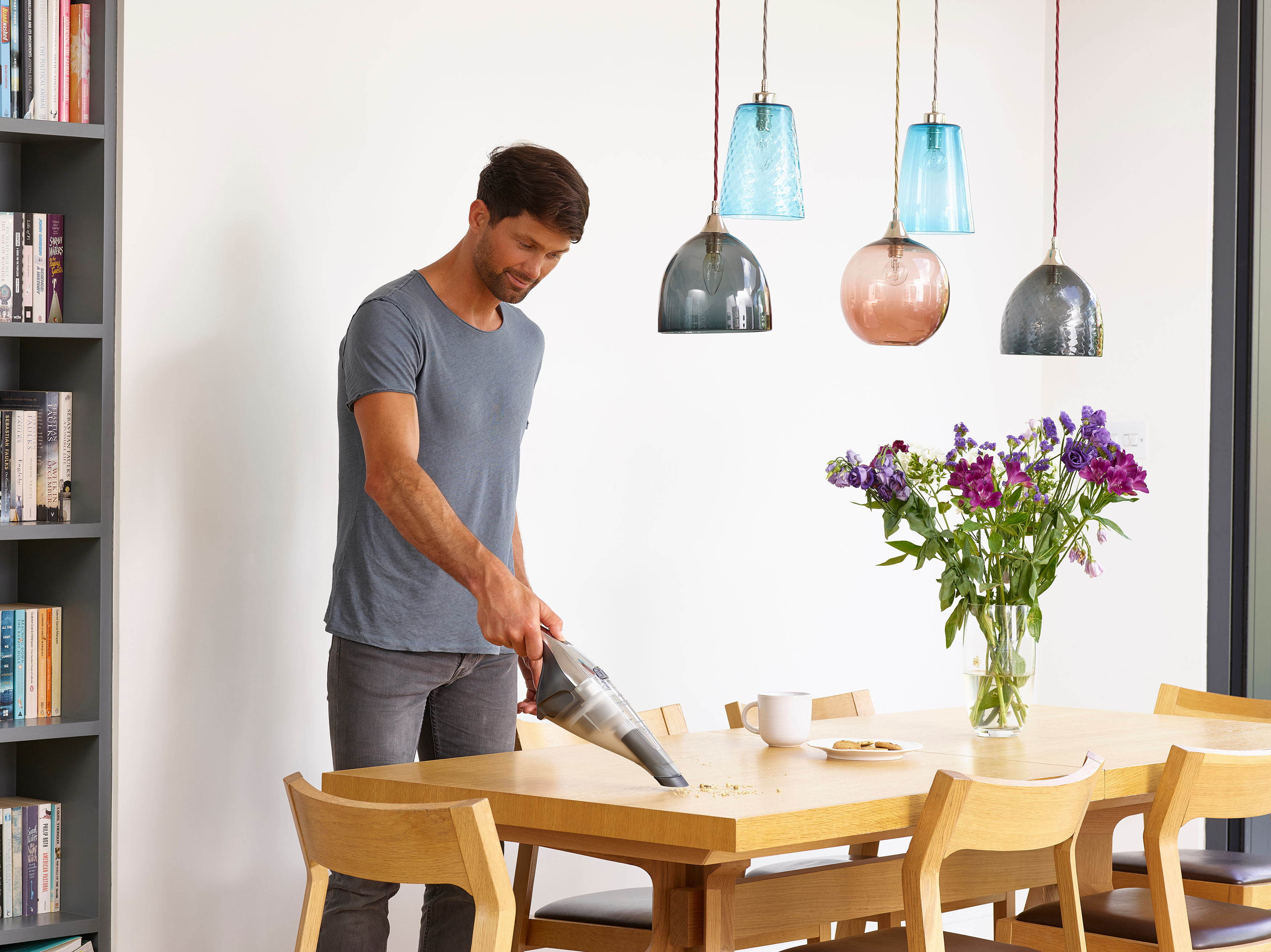 Mann, der einen Holztisch saugt. Blumen und Hängelampen im Hintergrund.