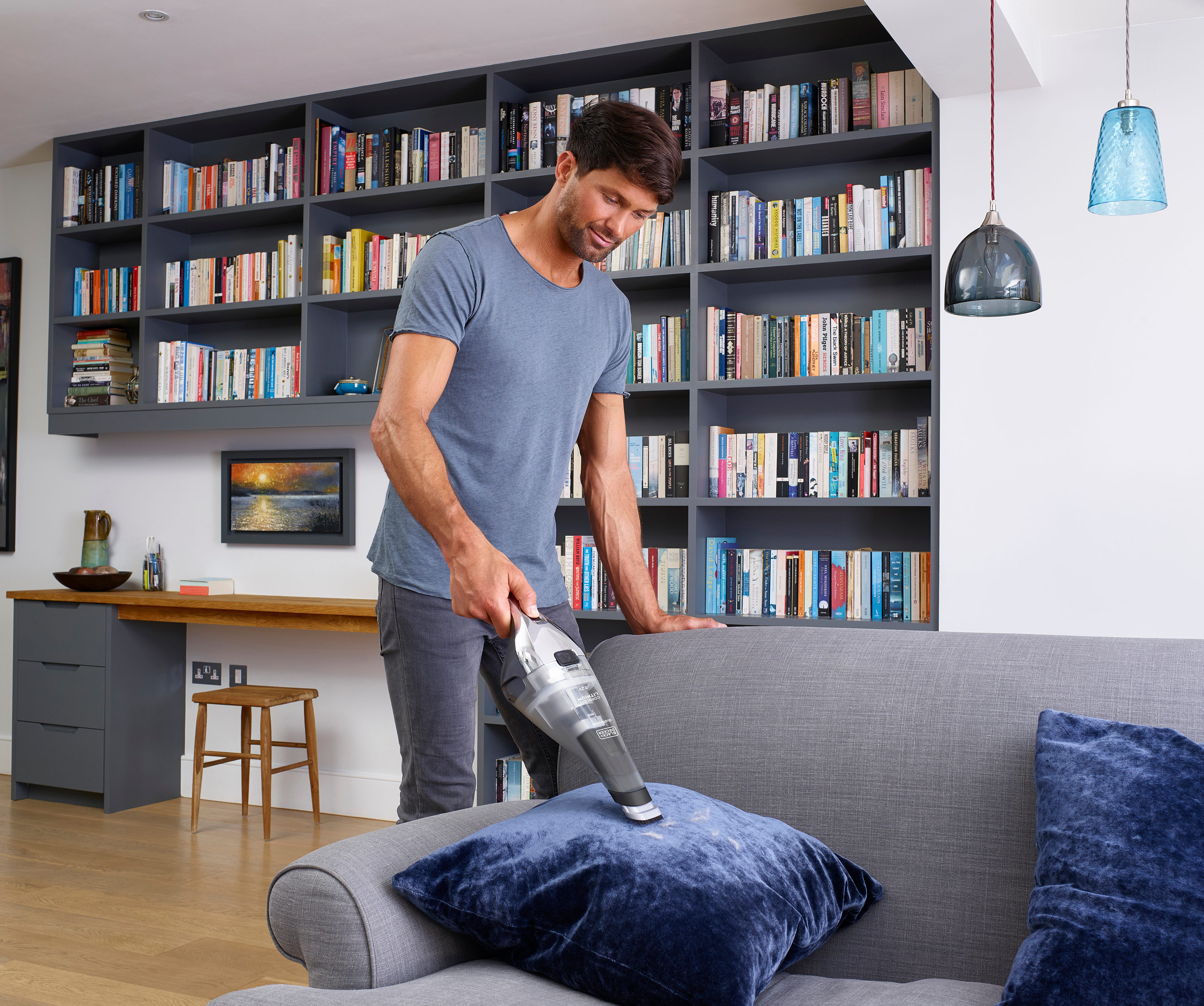 Ein Mann, der mit einem Handstaubsauger ein Sofa absaugt.