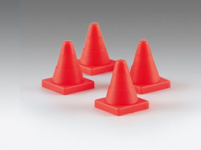 Vier rote Verkehrskegel. Sie sind klein, konisch und stehen auf quadratischen Sockeln. Weißer Hintergrund.