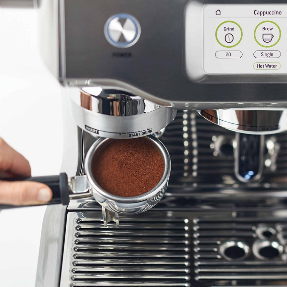 Espressomaschine mit gemahlenem Kaffee im Siebträger. Touchscreen zeigt Cappuccino, Mahlen, Brühen und Heißwasser.