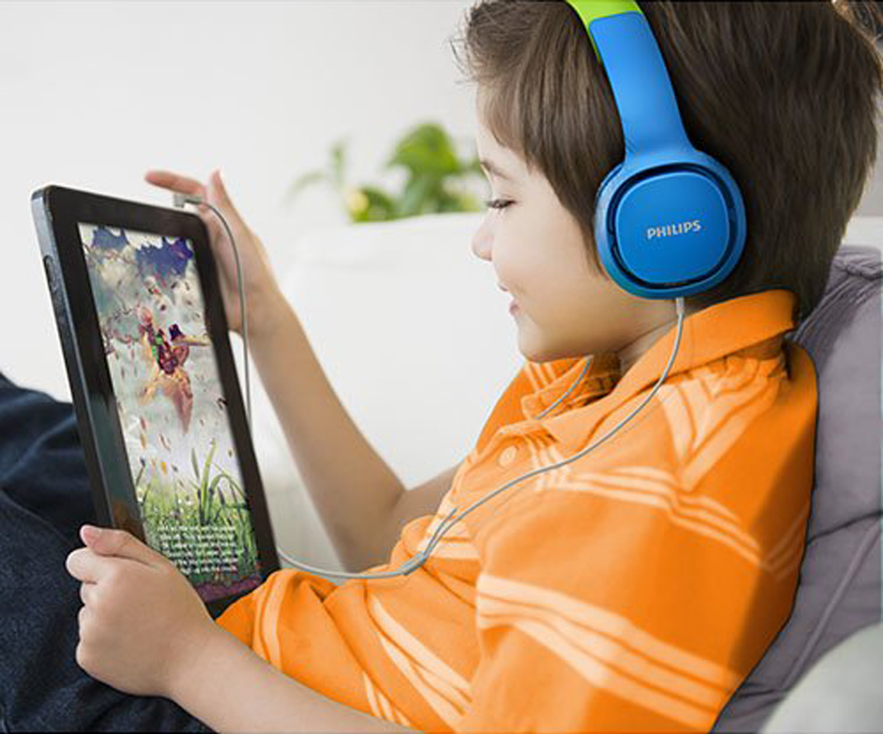 Een jongen met een blauwe koptelefoon, die een tablet gebruikt, met een oranje shirt.