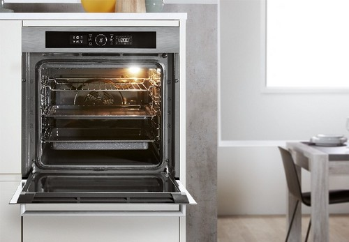Un horno abierto empotrado en un mueble blanco. En el interior, hay rejillas y luz.