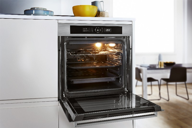 Un horno abierto con comida dentro. El horno está en una cocina blanca con una mesa y sillas al fondo.