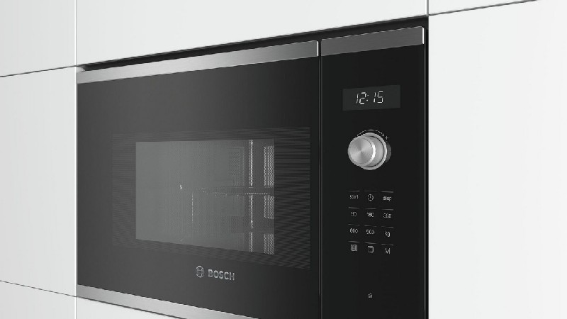 Un horno microondas negro con reloj digital y botones, empotrado en un armario blanco.