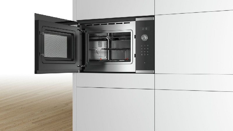 Un horno microondas abierto integrado en una cocina blanca. La puerta del horno está abierta, revelando el interior.